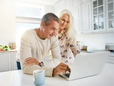 Middle-aged man and woman reading a computer screen on a white marble countertop in a modern kitchen, reviewing a guide on Florida probate real estate. Contact Kid Breukelen Realty Group for expert help.