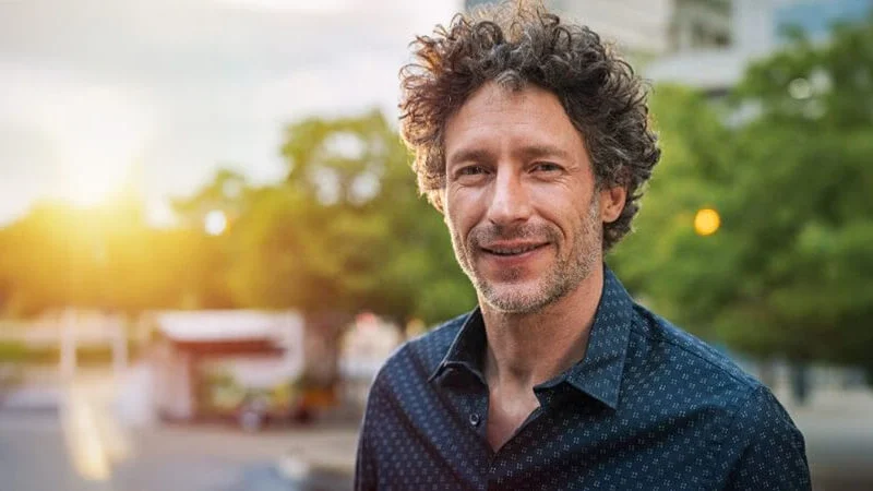 A man in a dress shirt standing outside with the sun over his shoulder, with a slightly blurred background. The image represents an out-of-state representative dealing with Florida probate real estate. Contact Kid Breukelen Realty Group for guidance