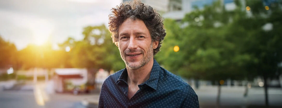 A man in a dress shirt, standing outside with the sun over his shoulder, and a slightly blurred background. The image represents an out-of-state representative managing Florida probate real estate. Reach out to Kid Breukelen Realty Group for expert help