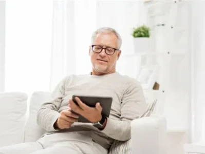Man sitting on a white sofa, reading a tablet in a white-themed room, reviewing essential probate real estate terms. Contact Kid Breukelen Realty Group for guidance.