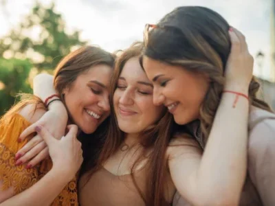 Three sisters hugging with a blurred high-rise background on a sunny day, symbolizing the resolution of probate property disputes. Contact Kid Breukelen Realty Group for guidance.
